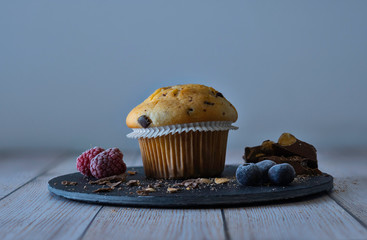 Muffin with nuggets and pieces of chocolate accompanied by blueberries and blackberries on the slate and old white wood.