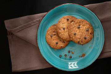 Oatmeal cookies and chocolate chips in ceramic plate on black background