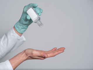a hand in a green medical glove applying a disinfectant or antiseptic gel to protect against infectious viruses, bacteria and germs, pours onto a hand without a glove on a white background