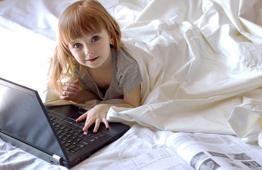 Distance online learning, a little girl sitting on the bed and studying on a laptop computer tablet digital book, preschool education modern technology, copyspace for text