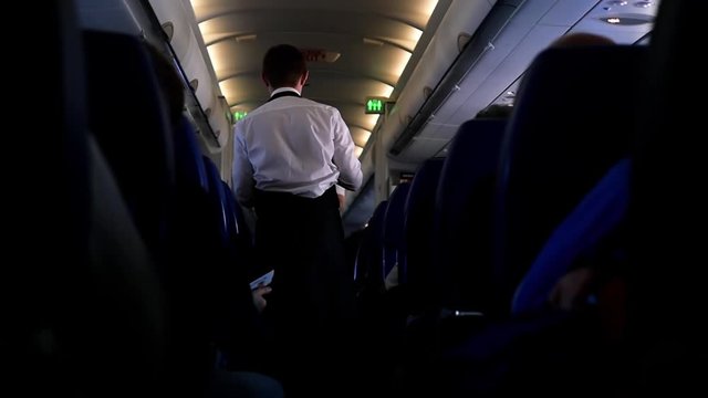 On board the flight are people on the plane and escorts in the aisle. Board the aircraft and the distribution of food. Cabin crew rear view