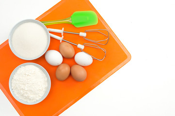 recipe step by step layout of products for biscuit on a sidikonovy orange rug 5 eggs, flour, vanilla sugar, sugar, baking powder, spatula and beaters for a mixer top view