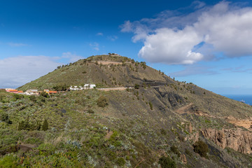 Fototapeta na wymiar View of the hilltop on a mountainous landscape of volcanic origin along with lots of trees on the horizon, one can see the setting moon of the Gran Canary island