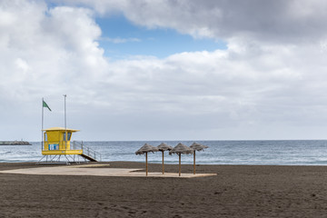 View of lifeguard tower on beach during windy sunny day with sea view and unique beach which has black sand on tower flutters green and yellow flag.