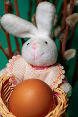 Toy rabbit holds a chicken egg in a basket. Easter bunny with egg