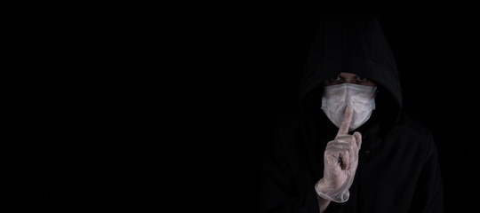 Close up profile portrait of man in the hood wearing medical mask and gloves. Dark background....