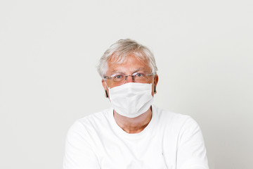 Old British guy at risk by coronavirus. Old grey hair guy wearing a face mask for protection against corona virus. Half body view of man wearing eye glass in paling white background with space 