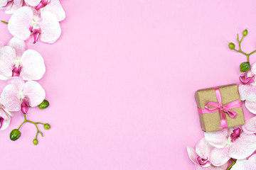 flat lay of present gift box with pink ribbon on pink background with orchid flower. spring concept. Copy space