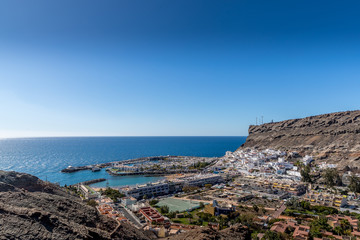 View from the air on the coast and bay in the city of Mogan on the Canary Islands where the bay harbor and people walking along the waterfront inside city