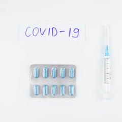 Novel coronavirus disease named COVID-19 written on paper with pills and syringe. Top view