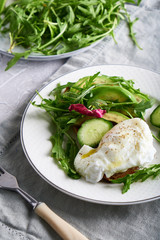 Poached eggs with herbs, avocado and cucumber served on a plate on a light background Copy space