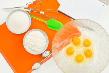 recipe step by step layout of products for biscuit on a sidikonovy orange rug 5 eggs, flour, vanilla sugar, sugar, baking powder, spatula and beaters for a mixer top view