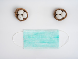 The celebration of Easter during the epidemic of the coronavirus. Easter eggs in a basket and a medical mask on white background.