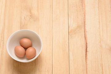 Three eggs and white cup on wooden background, top view and copy space for text