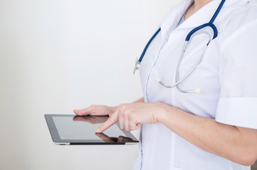 Unrecognizable female doctor in uniform uses a tablet computer. A medical worker contacts patients on a device. Cropped.