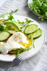 Poached eggs with herbs, avocado and cucumber served on a plate on a light background Copy space