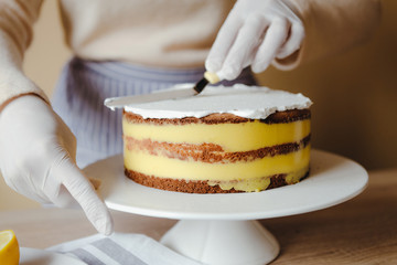 Housewife in the kitchen cooking a lemon cake with fruits, blackberry, lemon and mint on yellow background during quarantine. Recipe of organic homemade lemon cake. Concept of cooking at home.