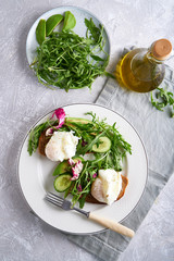 Poached eggs with herbs, avocado and cucumber served on a plate on a light background Copy space