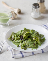 Green ravioli with peas and herbs on a white plate.