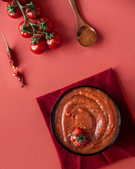 Tomato soup on a red background with tomatoes, top view.