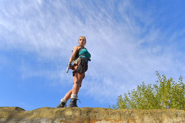 A young girl is dressed up in a military outfit.
She poses on a rock ledge in a stone quarry. 
She carries hand guns with her for self 
defense reasons.

