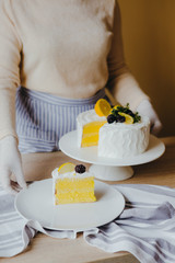 Housewife taking slice of fresh delicious birthday homemade lemon cake at table, top view. Concept of home cooking on qurantine. Recipe of lemon organic cake.