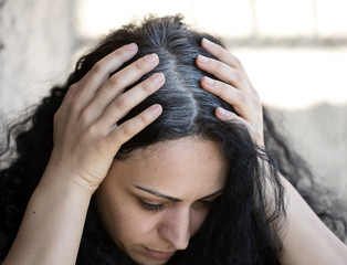 Woman is holding her head and checking white hair.