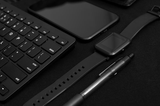 Composition with black pen, computer keyboard, smart watch, smartphone and leather wallet on dark black surface. Business concept. Business people items. Free space for text. Low key photo. 