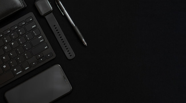 Flat lay composition with black pen, computer keyboard, smart watch, smartphone and leather wallet on dark black surface. Free space for text. Low key photo. Stationery. Items of successful people.
