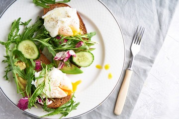 Poached eggs with herbs, avocado and cucumber served on a plate on a light background Copy space