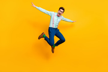 Fototapeta na wymiar Full size photo of cool stylish guy jumping high up rejoicing good mood wear specs shirt bow tie suspenders trousers shoes green socks isolated bright yellow color background