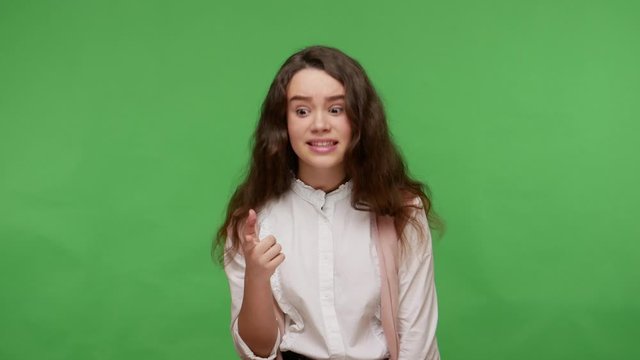 Hey you! Astonished teenage brunette girl in white shirt pointing at camera, blaming for mistake and looking with amazed resentful expression, shocked by bad result. indoor studio shot, isolated