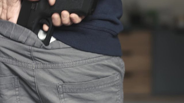 Close up of a young boy placing a nine millimeter toy gun perfect replica on the back of his pants and then hiding it under his sweatshirt