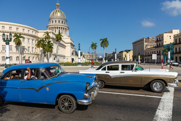 Brightly colored classic American cars serving as taxis pass on the main street in front of the Capitolio building in Central Havana, Cuba.