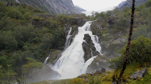 Waterfall and river which is located near path to the Briksdalsbreen (Briksdal) glacier. The melting of this glacier forms waterfall and river with clear water. Jostedalsbreen National Park. Norway.