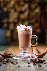 Side view tasty hot cocoa chocolate with whipped cream with marshmallows in a glass mug on a wooden background, vertical