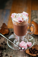 Tasty hot cocoa chocolate with whipped cream with marshmallows in a glass mug on a wooden background, vertically