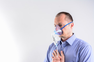 Mid adult man wearing oxygen mask, studio shot. Portrait of man wearing an inhalation mask isolated on white background. Man Inhaling Through Inhaler Mask.