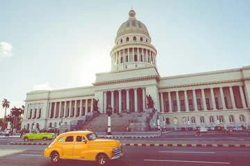 Poster Brightly colored classic American cars serving as taxis pass on the main street in front of the Capitolio building in Central Havana, Cuba. © Curioso.Photography