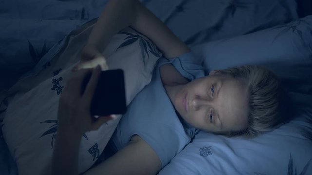 vertically. woman suffering from insomnia uses a smartphone while lying in bed
