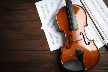 Fototapeta premium Beautiful violin, bow and note sheets on wooden table, flat lay. Space for text