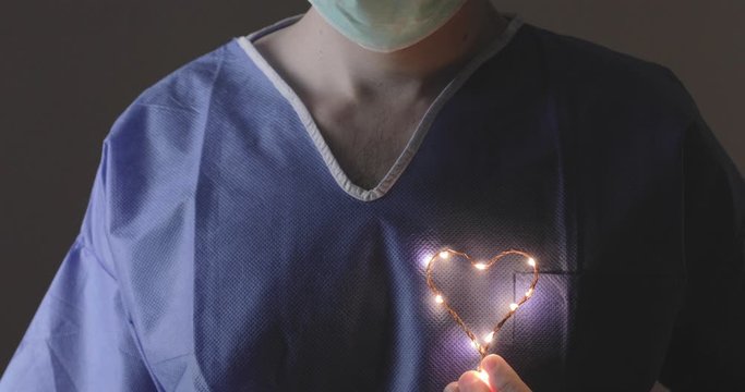 Occhi in primo piano di un medico in prima linea alla lotta al Coronavirus tiene in mano un piccolo simbolo del cuore luminoso per dare speranza alla fine della pandemia Coroanvirus.