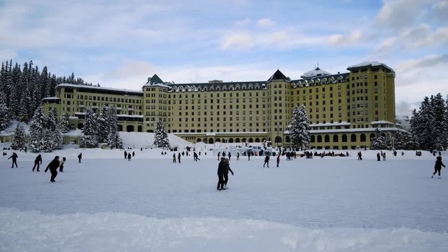 People  Ice Skating In The Frozen Lake Louise Located In Front Of Luxury Resort Of Fairmont Chateau Lake Louise. wide shot