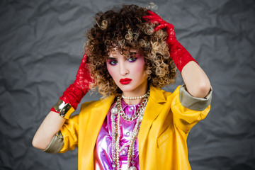 Portrait of a girl in a yellow jacket and blue jeans with afro hair of the eighties, disco era. Photo in studio on a gray background.