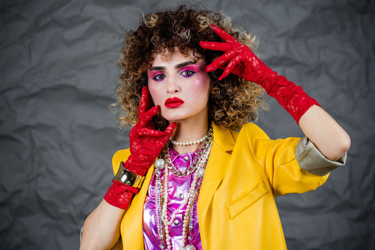 Portrait of a girl in a yellow jacket and blue jeans with afro hair of the eighties, disco era. Photo in studio on a gray background.