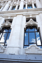 Obraz premium The fragment of the white stone house’s facade with windows and reflections of blue sky and clouds in it.