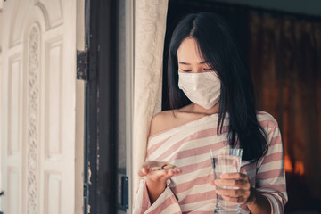 Young woman looking drug and wearing mask with medicine putting on hand and a glass of water, Pharmaceutical medicament, cure in container for health, Antibiotic, Medicine and health care concept.