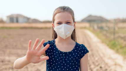 Coronavirus and air pollution concept. Little Caucasian girl wearing face mask for protection - child making stop gesture