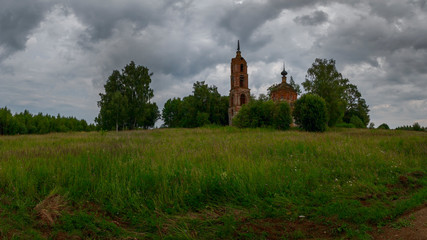 Fototapeta na wymiar A cloudy landscape with an abandoned Church standing among trees. Ivanovo region, Russia.
