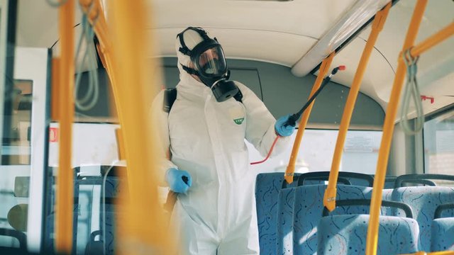 Person in protective suit sprays chemicals, disinfectant. Sanitary inspector is doing a disinfection inside of a bus